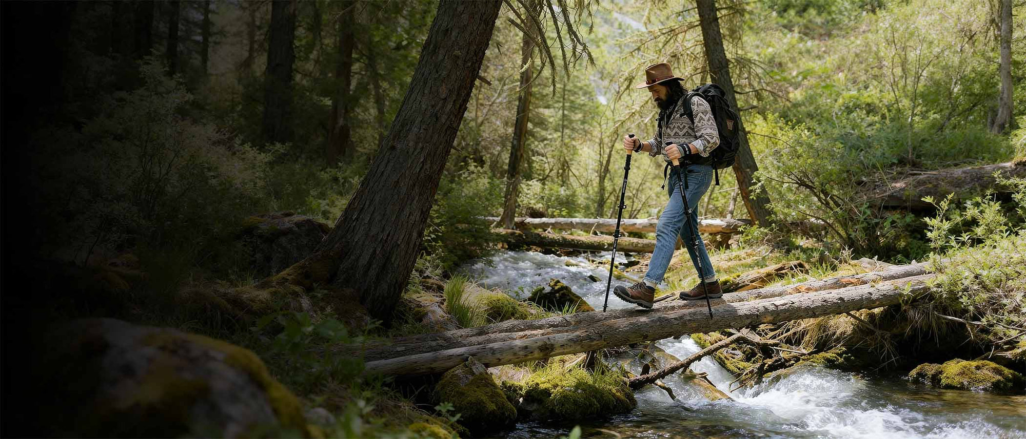 Person hiking through a forest with a backpack and walking sticks over a stream.