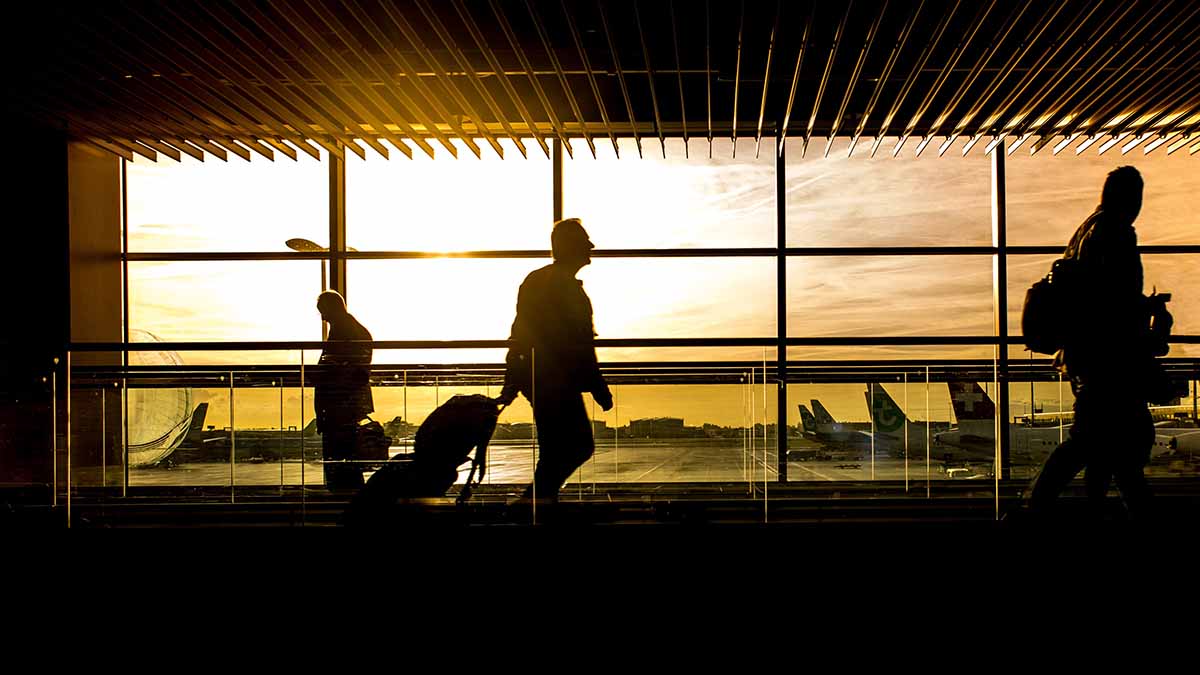 A silhouette photo of travelers walking through a spacious airport terminal at sunset, representing the typical pre-flight environment where understanding TSA carry-on baggage policies for specific items like trekking poles is critical.